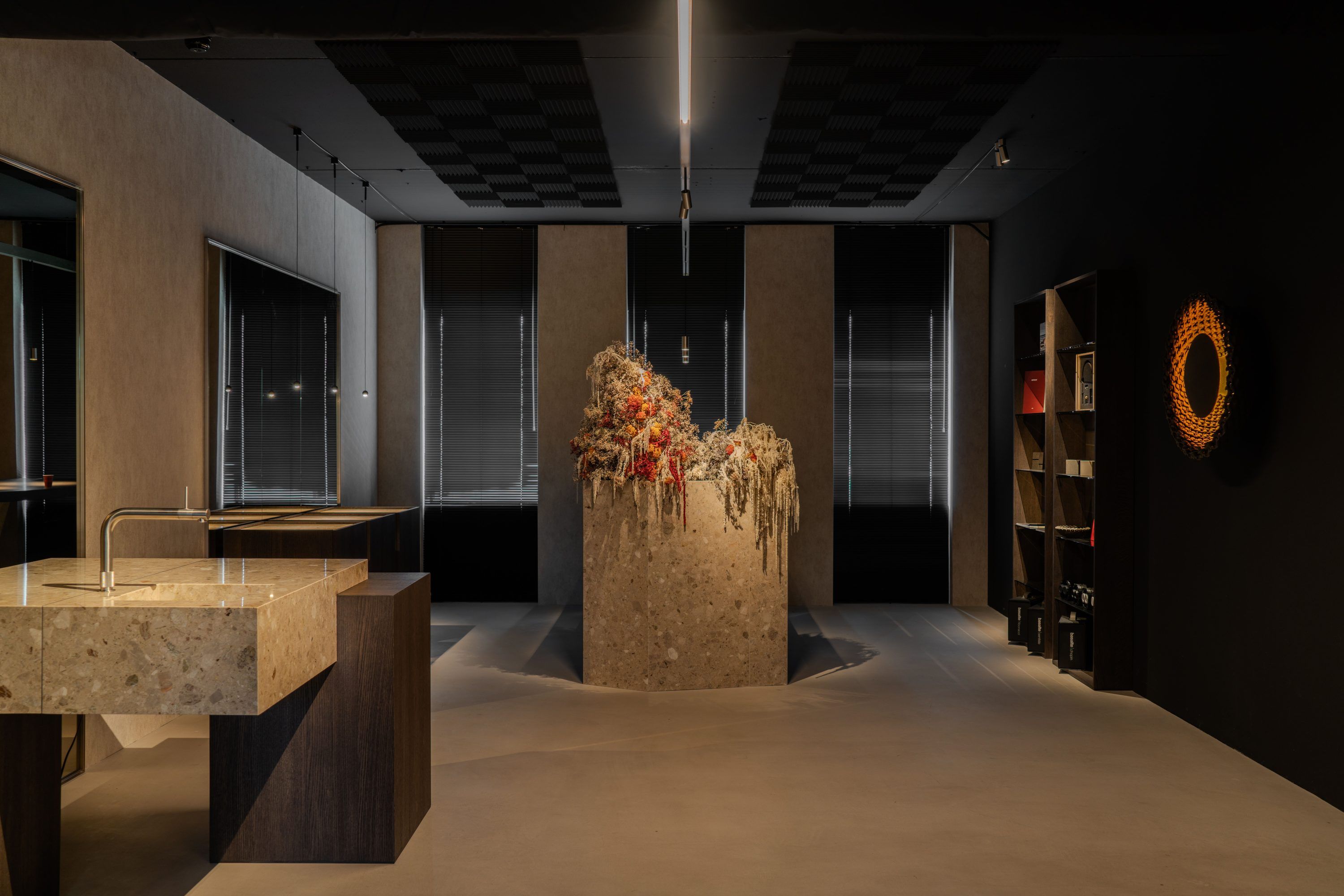 De showroom van Contrast Lighting in Capelle aan den IJssel: een terrazzo wastafel, een zuil met droogbloemen, vitrines langs de ramen en een ronde wandlamp tegen een zwarte wand