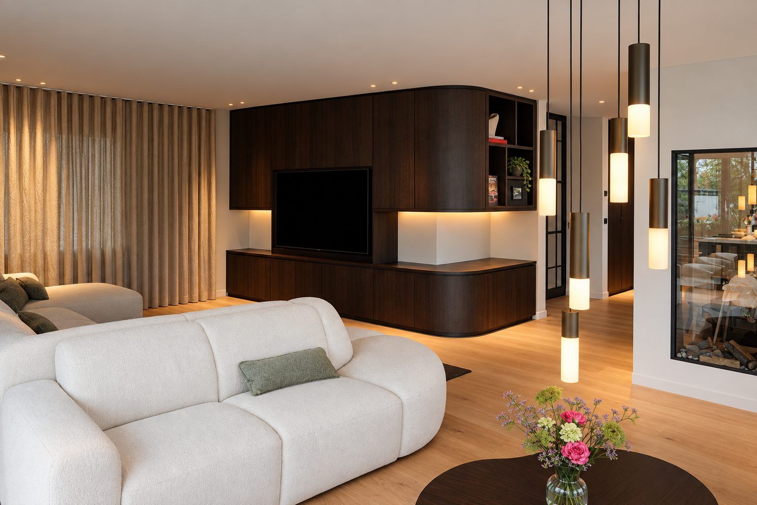 Woonkamer met een witte bank, een donkere houten kastenwand met verborgen licht en een cluster van smalle cilinderhanglampen, met inbouwspots in het plafond