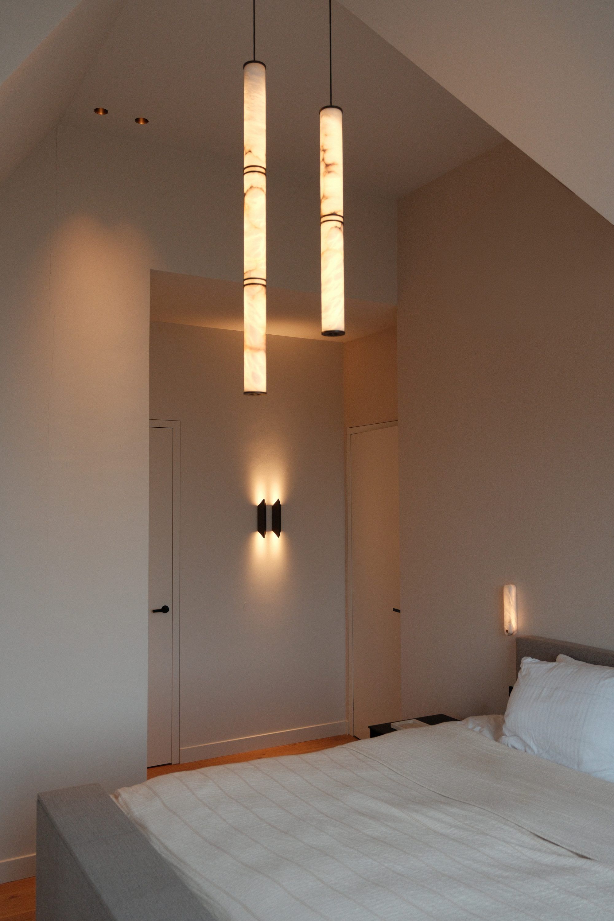 Slaapkamer onder een schuin dak met twee hanglampen van albast in de nok en een wandlamp tussen twee deuren