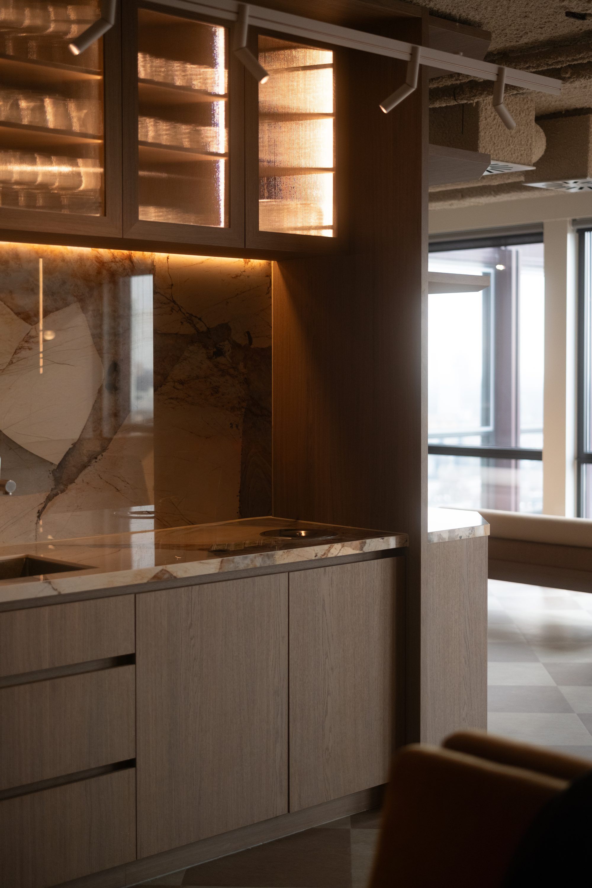 Pantry met een marmeren achterwand, verlichte glazen bovenkasten en spots op een rail