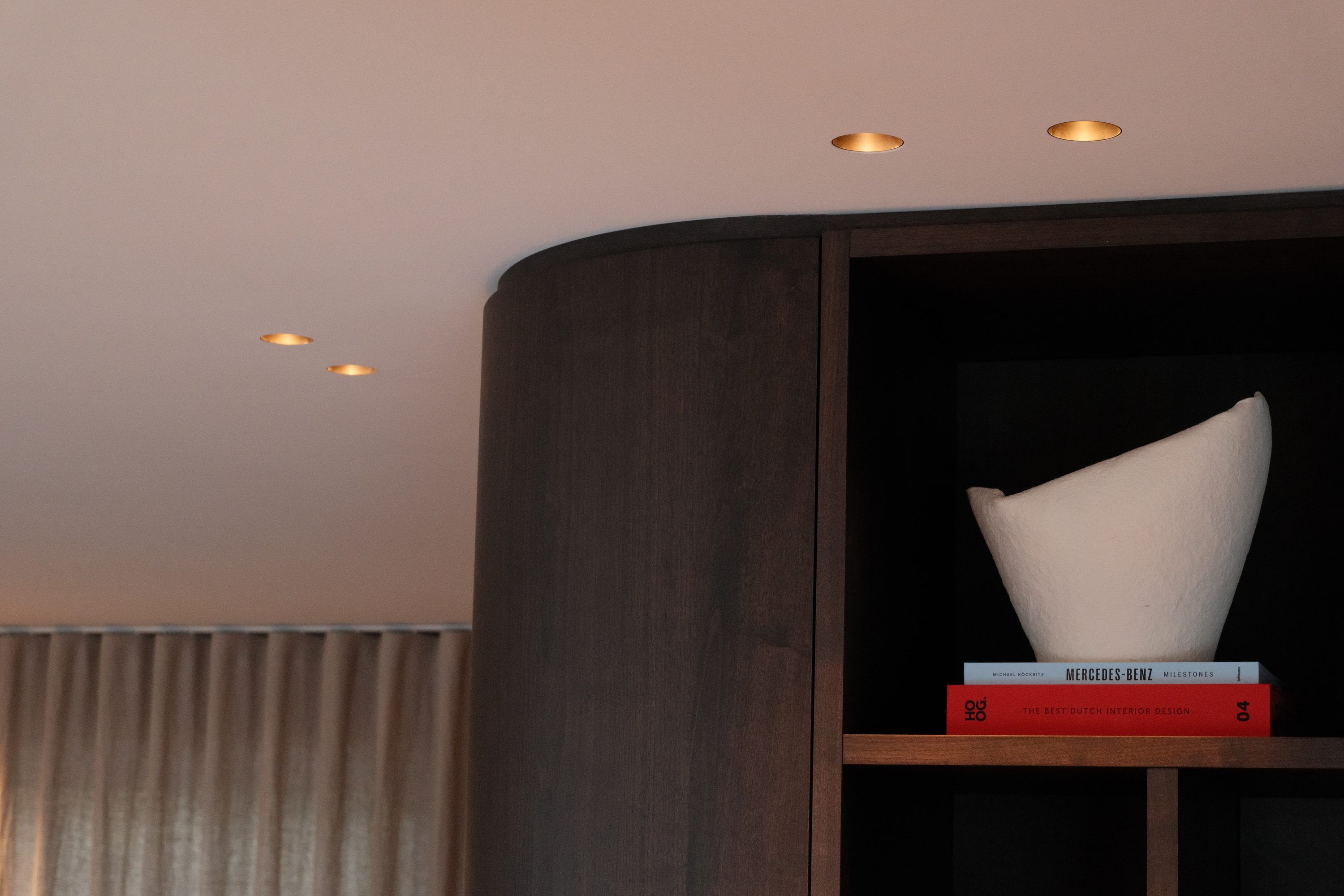 Donkere houten kast met een ronde hoek onder inbouwspots, met een wit object op een plank