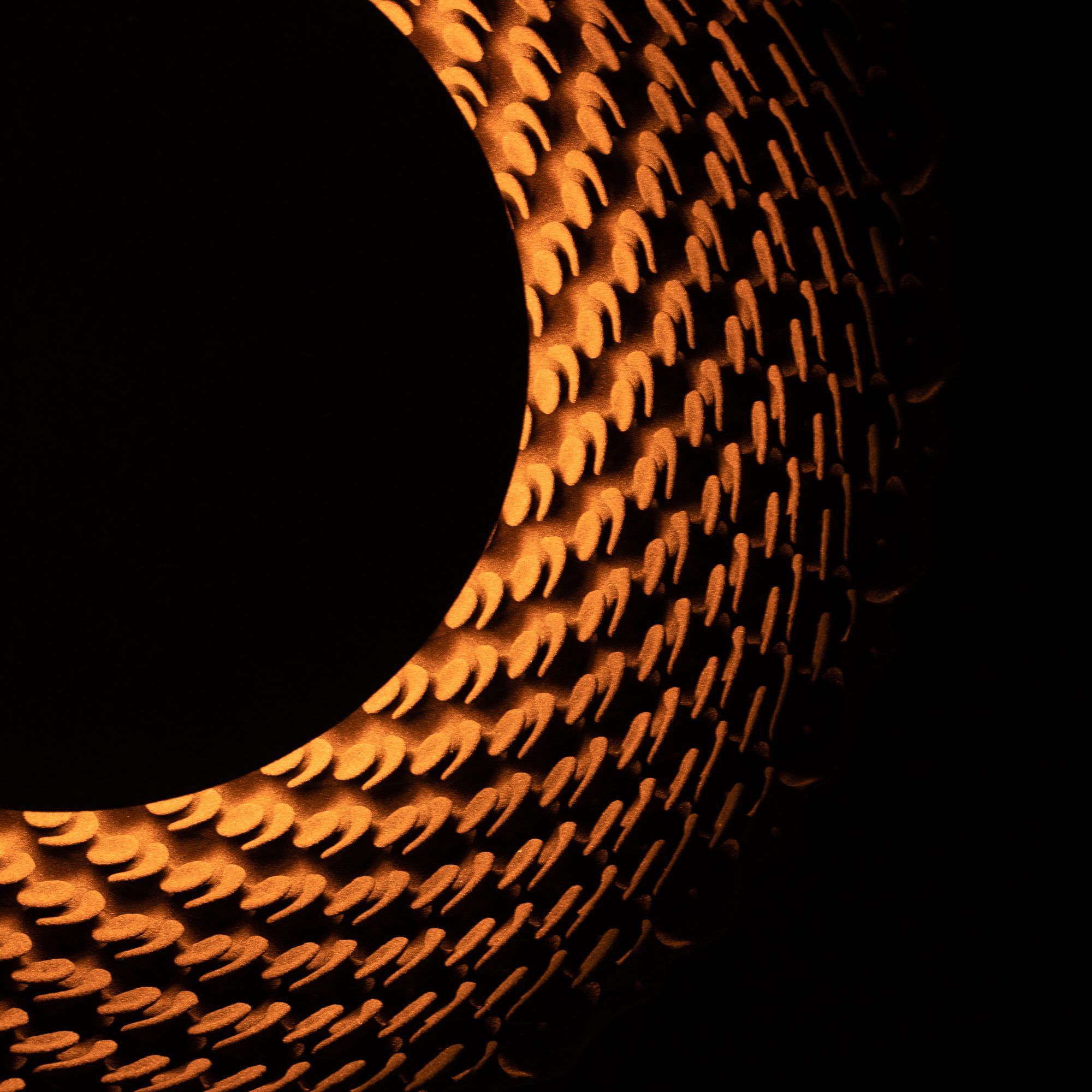 Detail van een Sun-lamp in het donker: warm licht valt door het reliëf van schubben rond een zwarte schijf